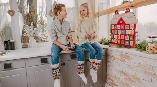 Kinderen zitten bij een huisvormige adventskalender en openen vakjes